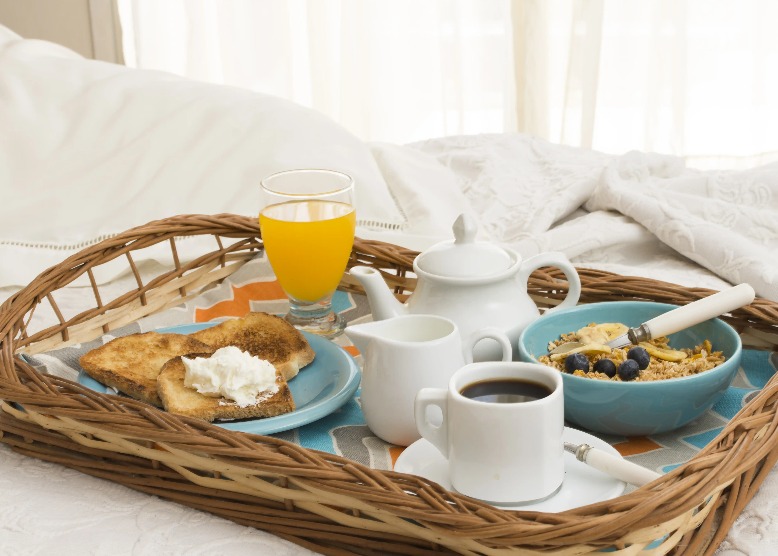 Breakfast variety on bed including fruits, cereal, coffee, and a juice